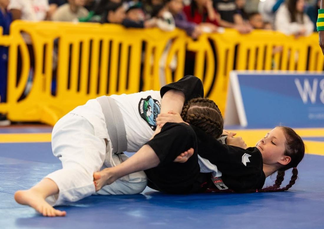 Two young jiu-jitsu competitors grappling on a mat